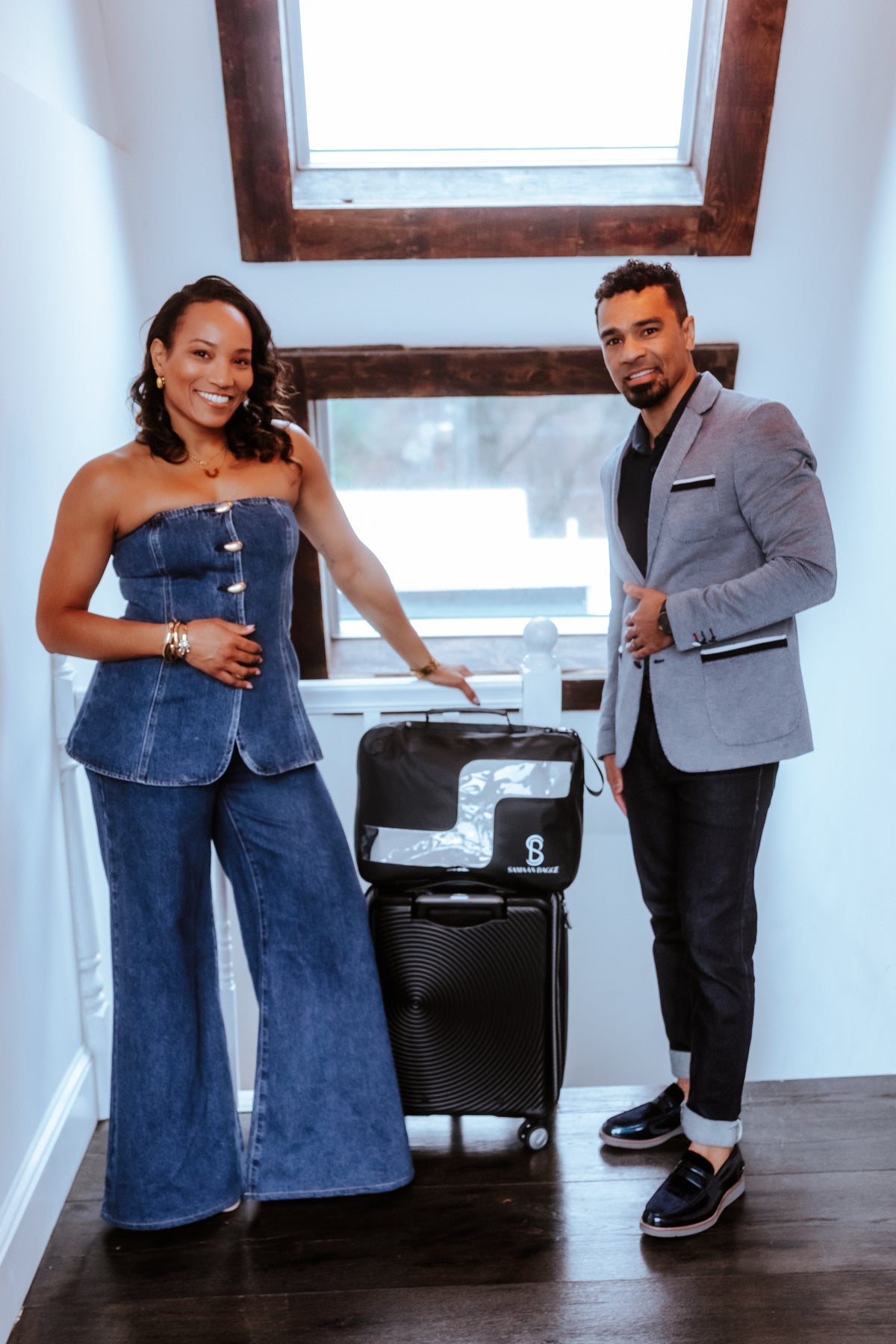 Two people standing with a suitcase in a room with a window.
